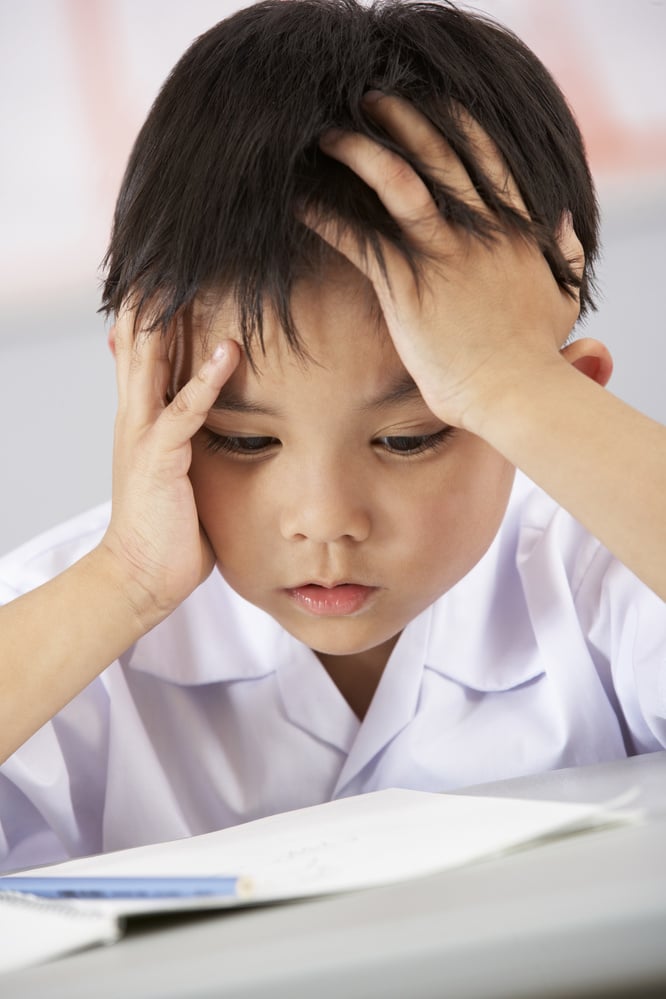 Unhappy Male Student Working at Desk in Chinese School Classroom